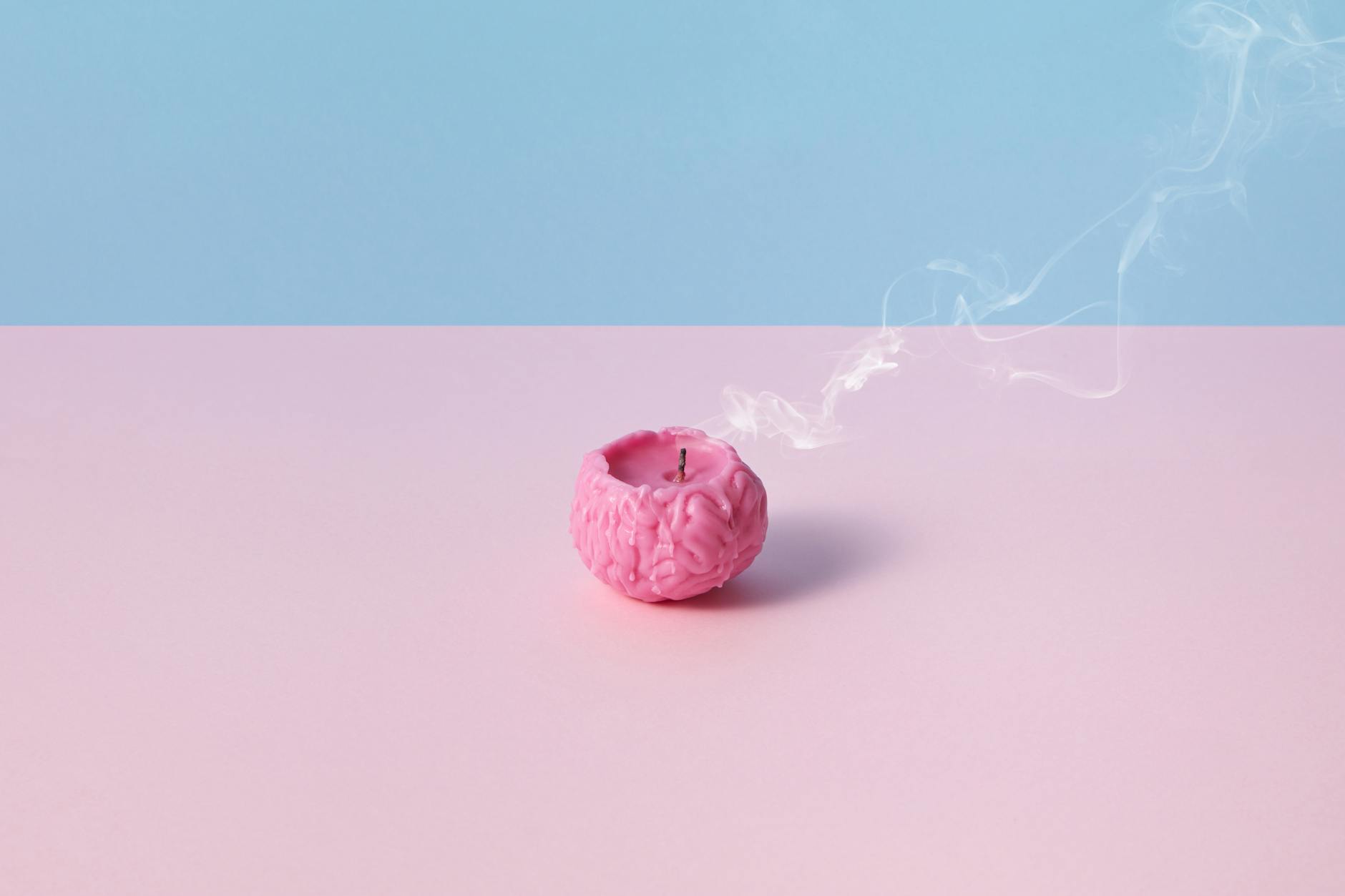 Różowa świeca w kształcie mózgu dymiąca na pastelowym tle