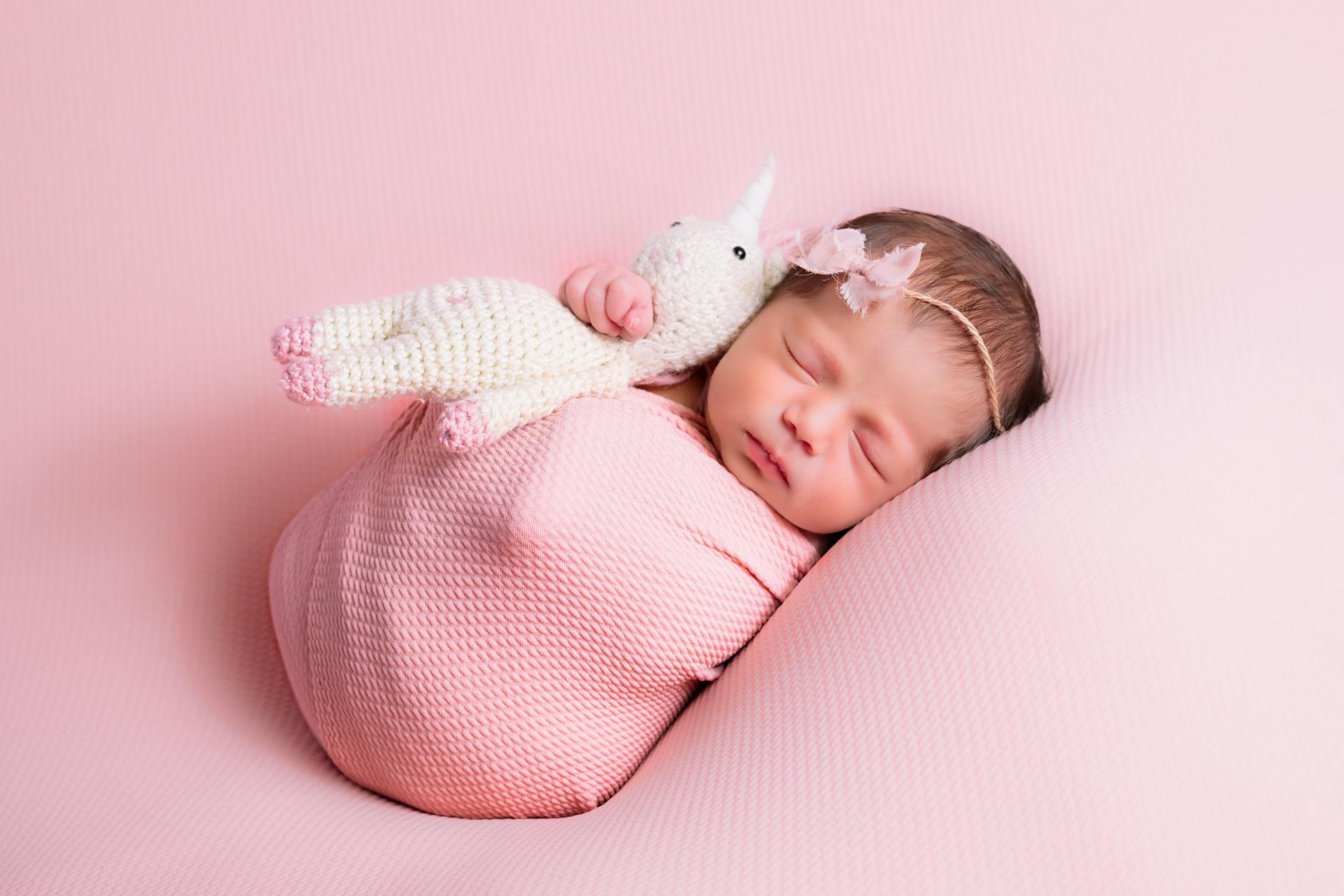 Śpiący noworodek w różowym kocyku z pluszowym jednorożcem