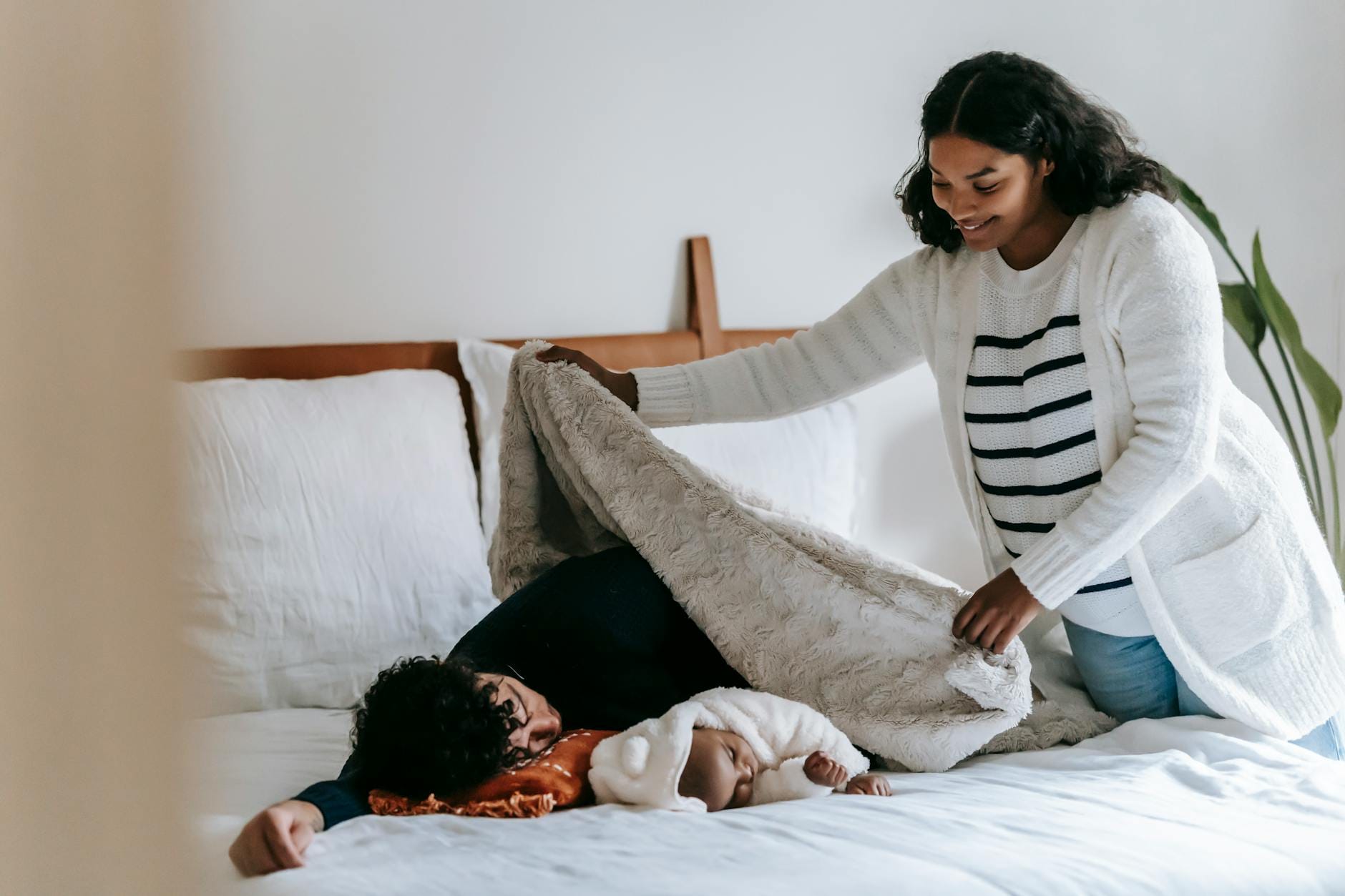 Mama okrywa śpiącego tatę z niemowlęciem ciepłym kocem na łóżku
