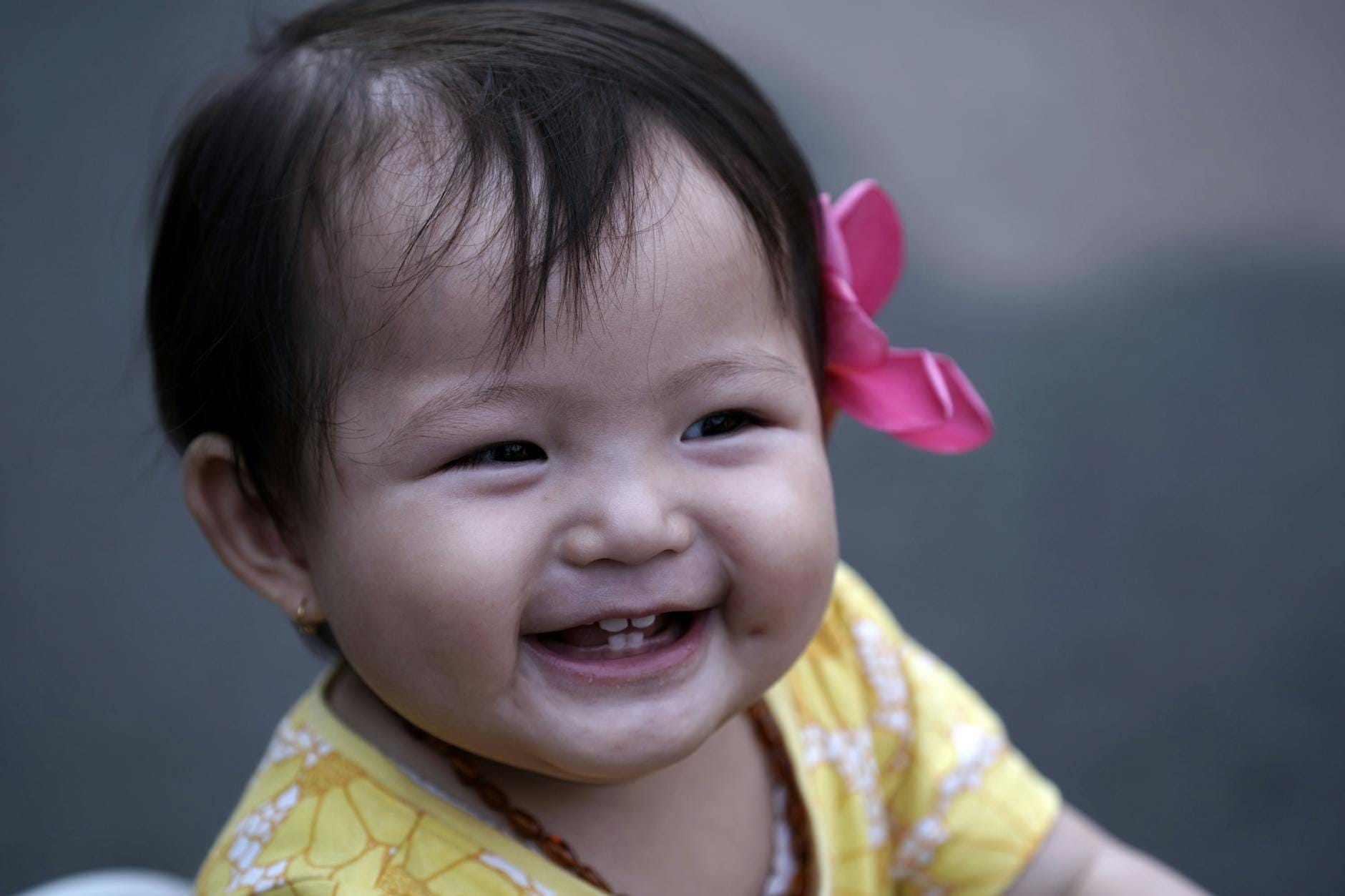 Uśmiechnięte niemowlę w żółtej sukience i różowej kokardce na głowie