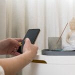 Kobieta ze smartfonem obok figurki Buddy i kadzidła w domowym zaciszu