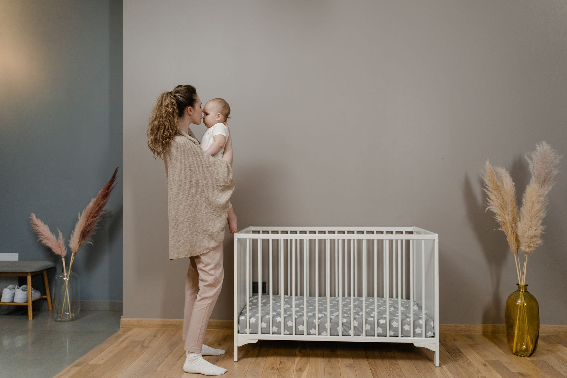 Mama trzyma śpiące niemowlę obok łóżeczka w przytulnym pokoju